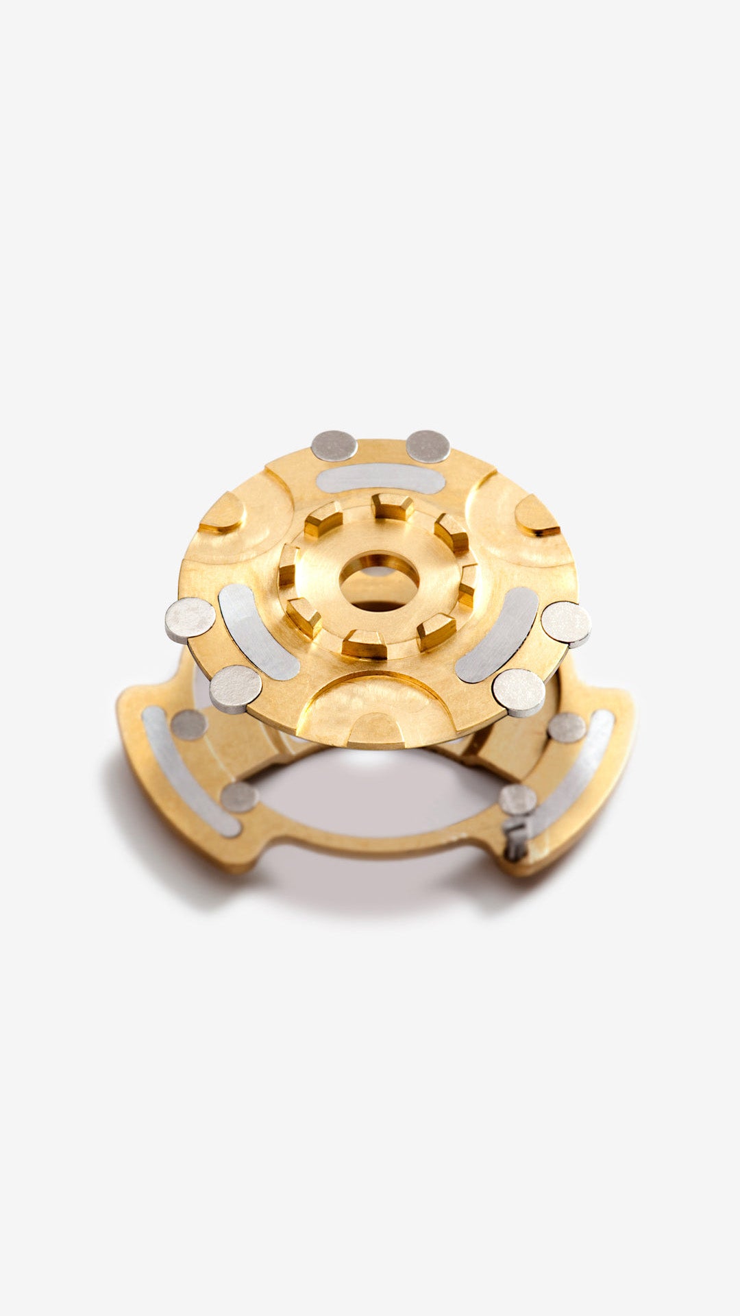 Gold and silver mechanical component used for Ressence's magnetic transmission on oil-filled watches on a white background, vertical image