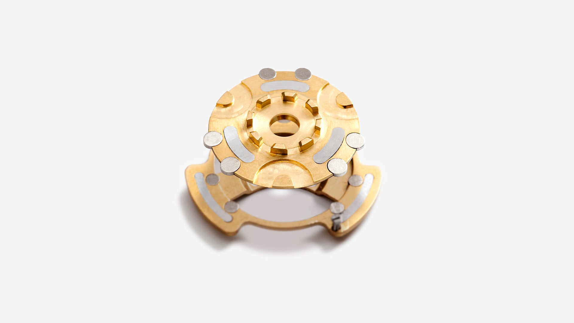 Gold and silver mechanical component used for Ressence's magnetic transmission on oil-filled watches on a white background.