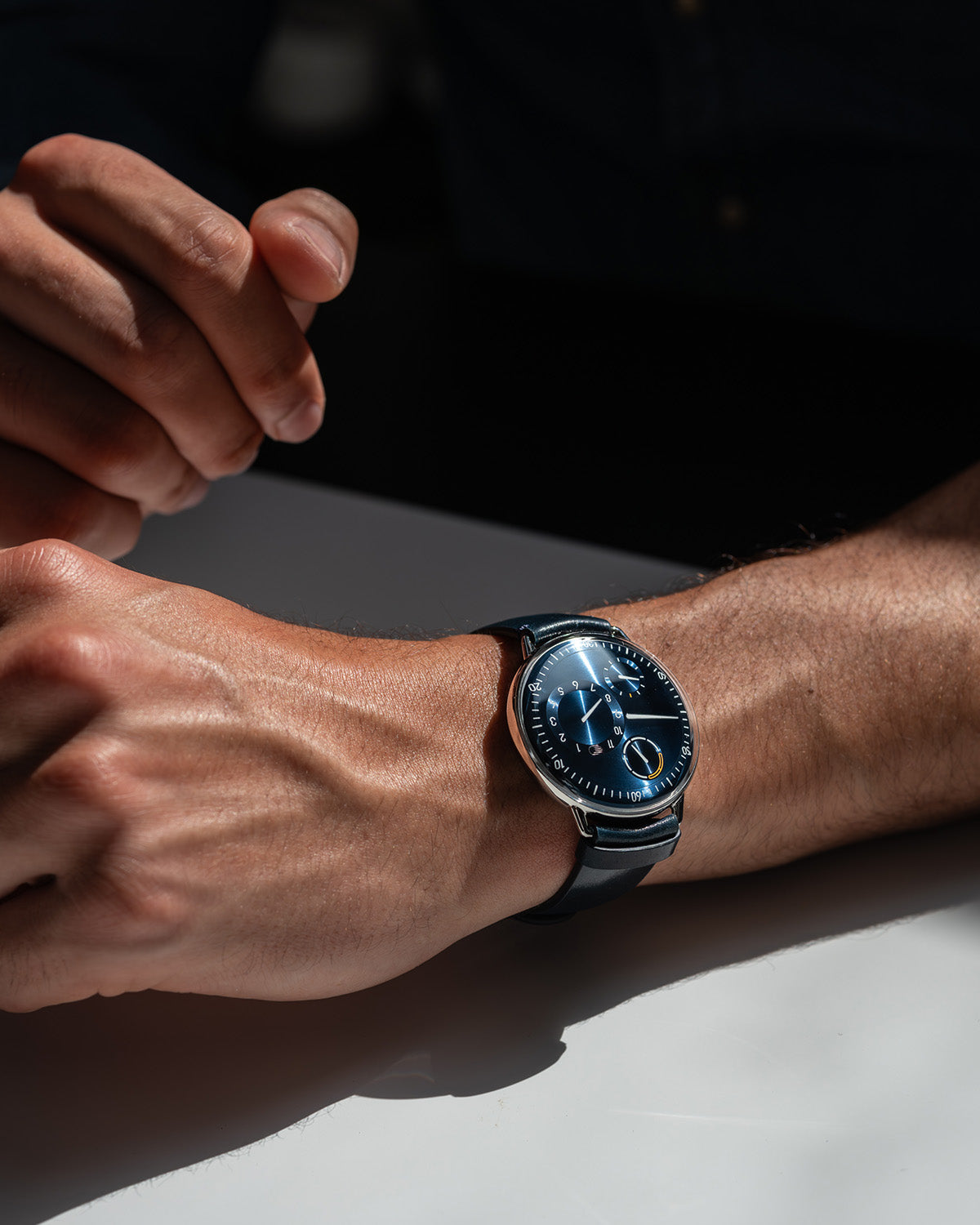 Vertical image of a Ressence TYPE 1 Round Night Blue, the essential titanium watch, shown dial-up on a man's wrist