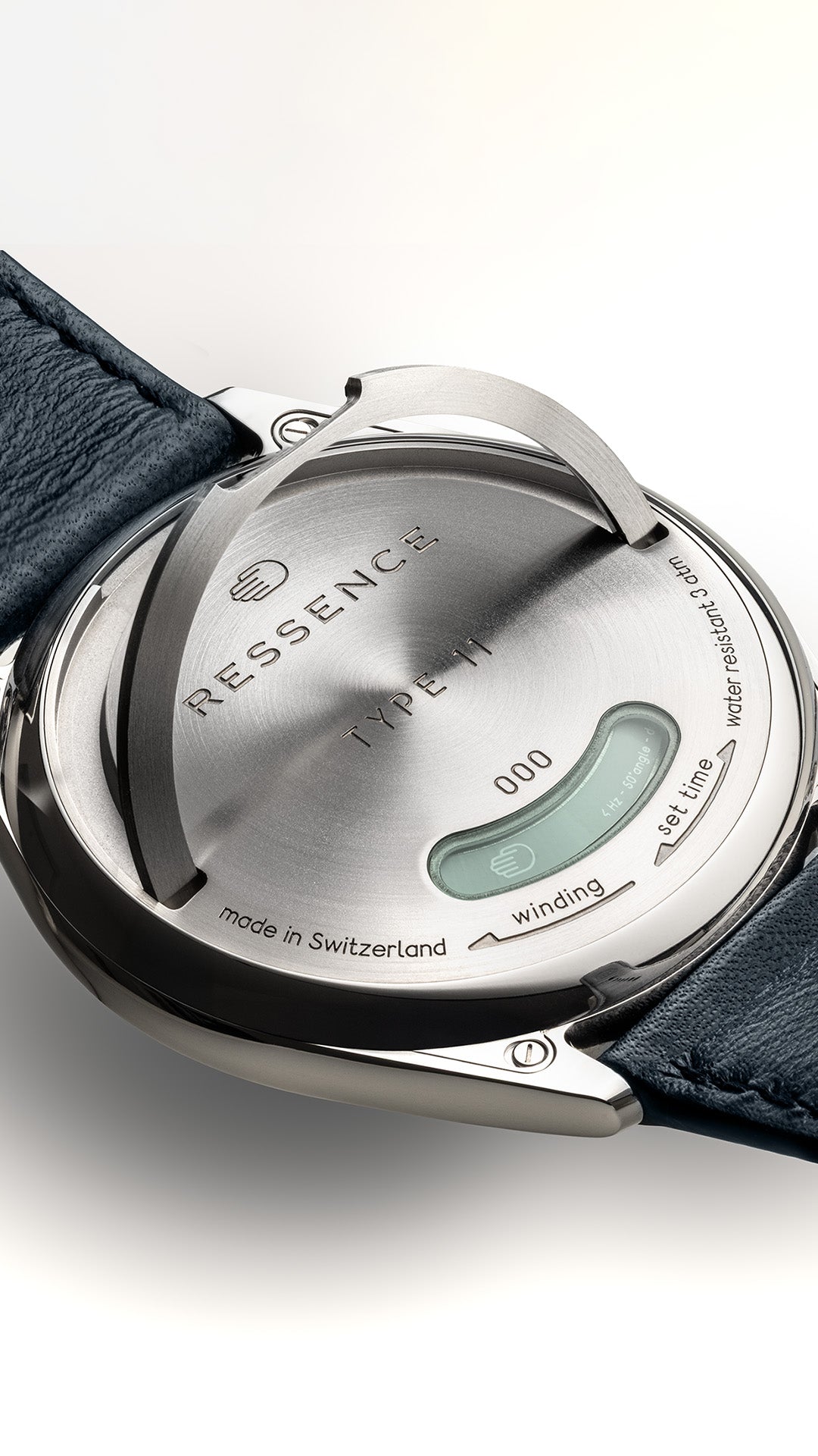 Vertical close-up of a Ressence TYPE 11 watch's caseback with the lever to set and wind the watch lifted up, with a blue strap on a white background