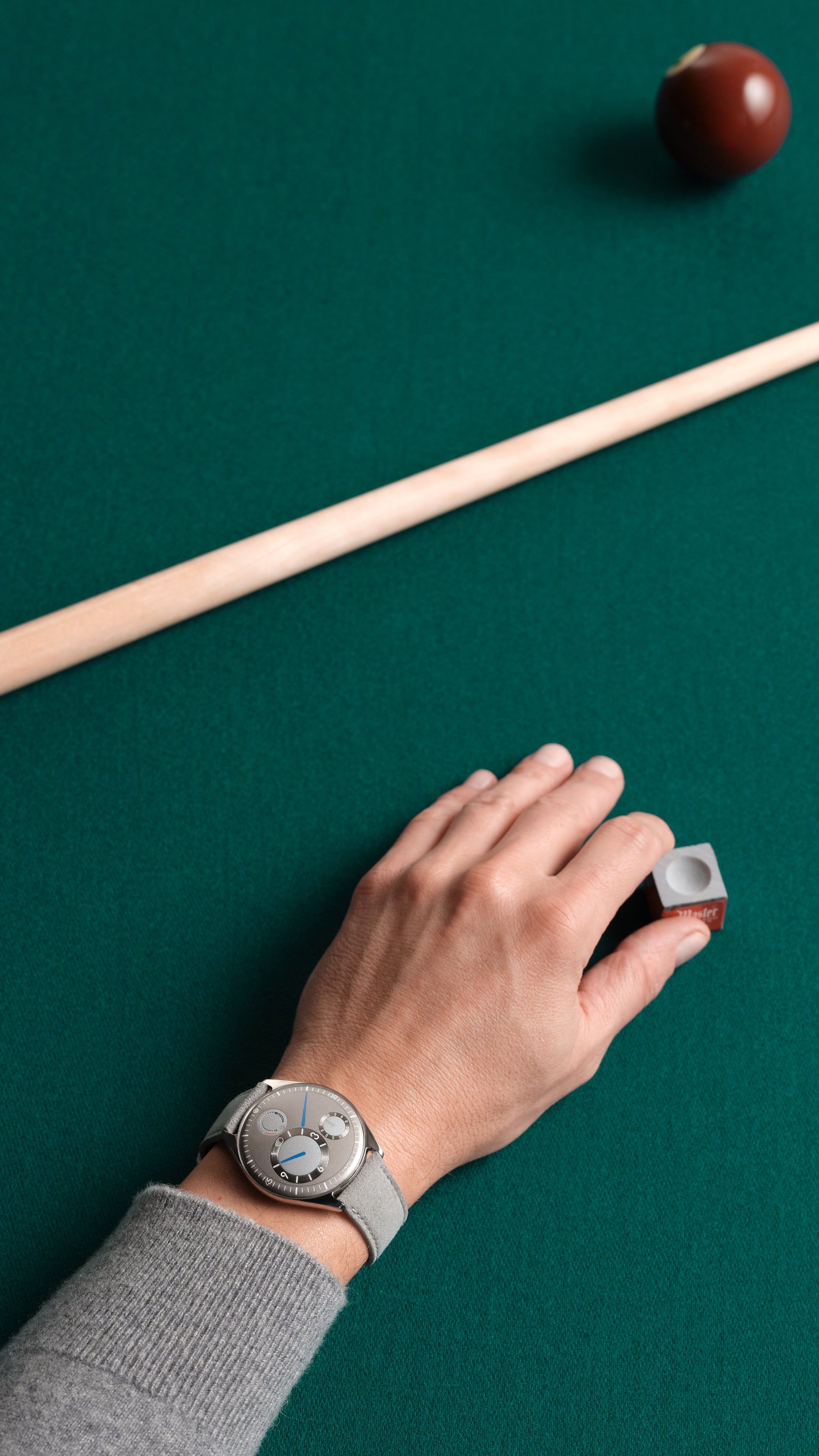 Ressence TYPE 11 Latte, a contemporary watch, shown on the wrist of a snooker player on a green table. vertical image