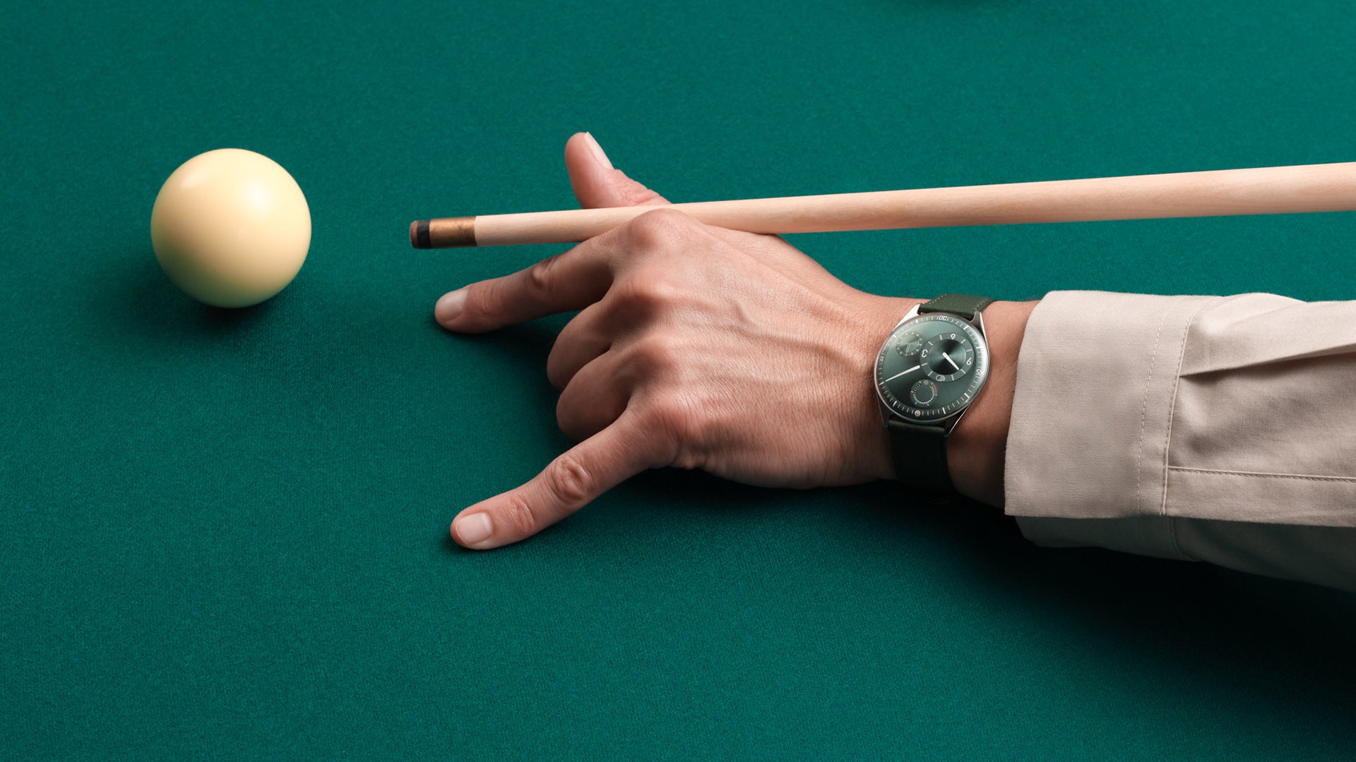 Hand holding a pool cue approaching a ball on a green pool table wearing a Ressence TYPE 11 Pine, a contemporary luxury watch on the wrist