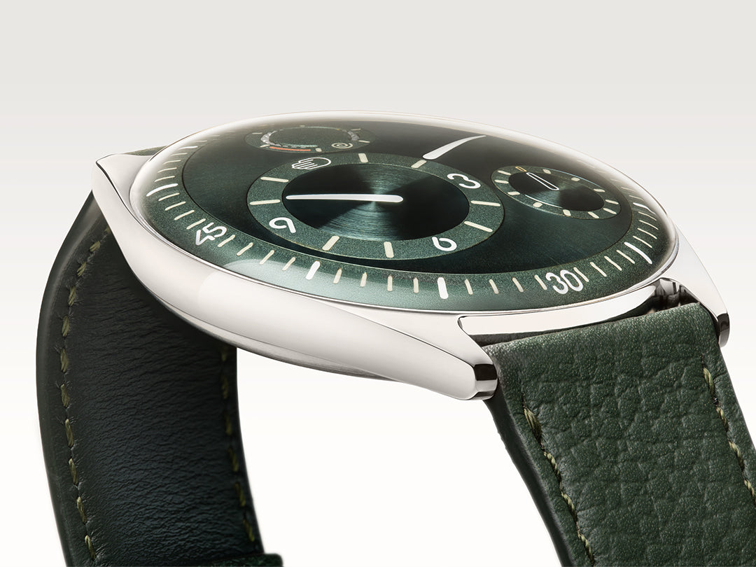 Ressence TYPE 11 Pine, a contemporary watch with a green dial and green leather strap, shown dial-up on the side. vertical image.