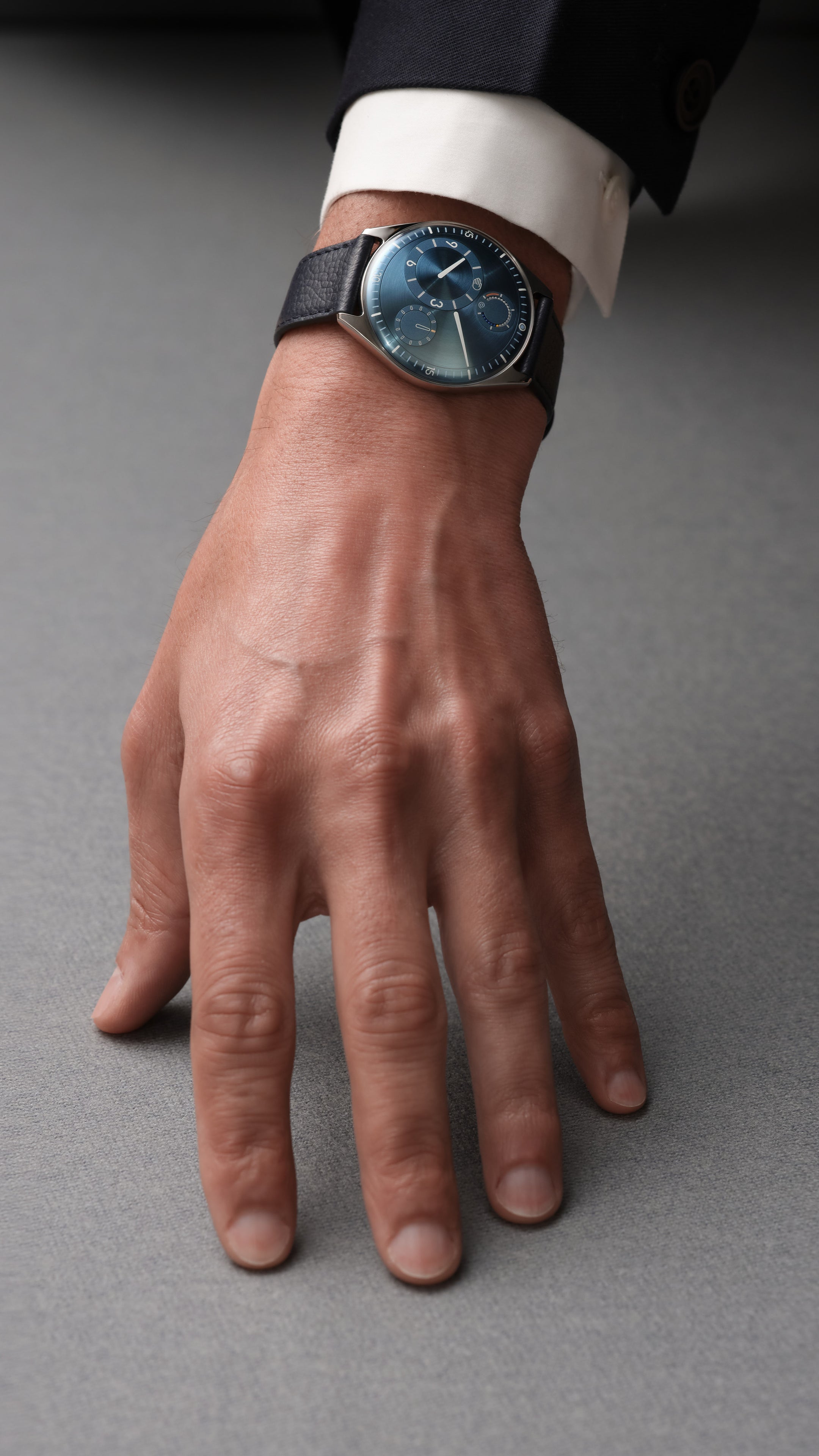 Vertical Close-up of a wrist wearing a luxury Ressence TYPE 11 Sky with a dark blue leather strap and detailed face, against a neutral background.