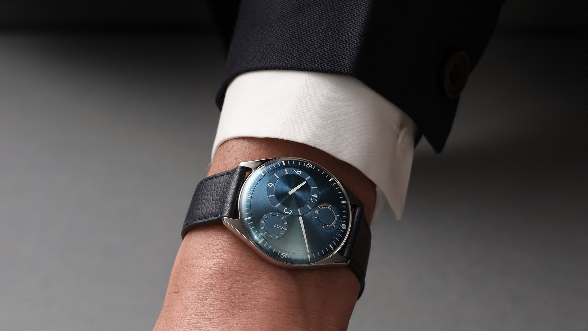 Close-up of a wrist wearing a Ressence TYPE 11 Sky with a dark blue leather strap and detailed face, against a neutral background.
