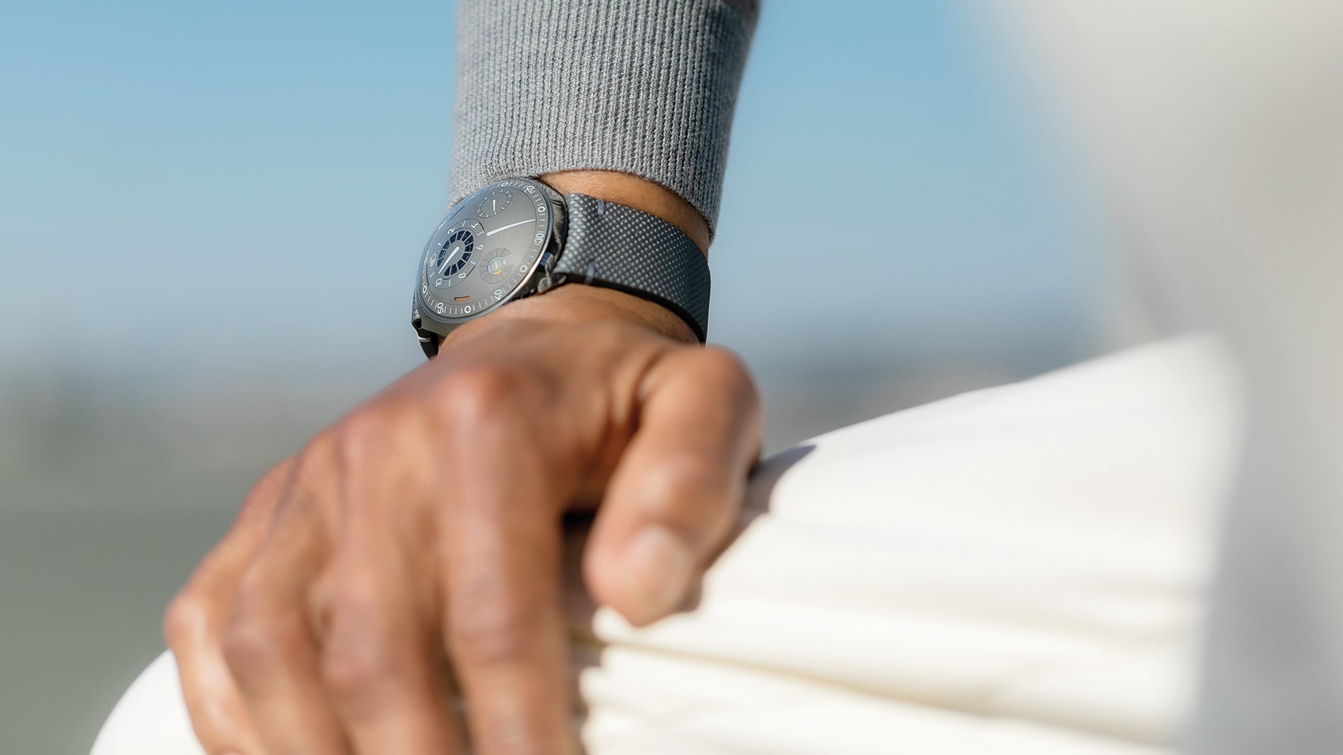 Person wearing a Ressence TYPE 2 connected watch with their hand resting on their knee with a blurred background