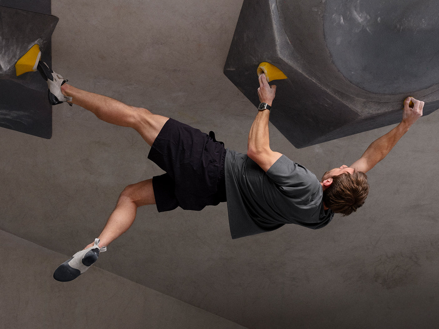 Person climbing on a rock wall with a focus on their climbing technique and wearing a Ressence TYPE 7 Black sport-chic GMT titanium watch