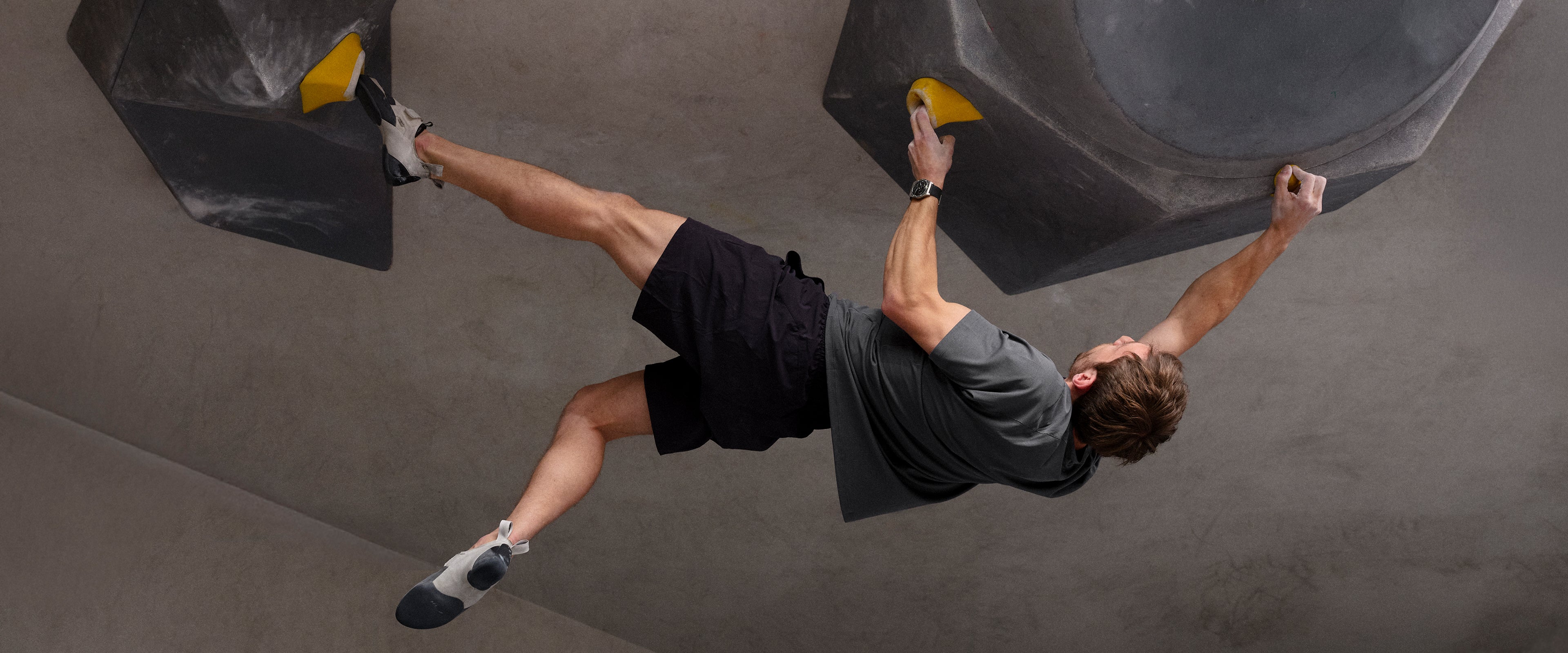 Person climbing on a rock wall indoors wearing a Ressence TYPE 7 Black sport-chic GMT titanium watch