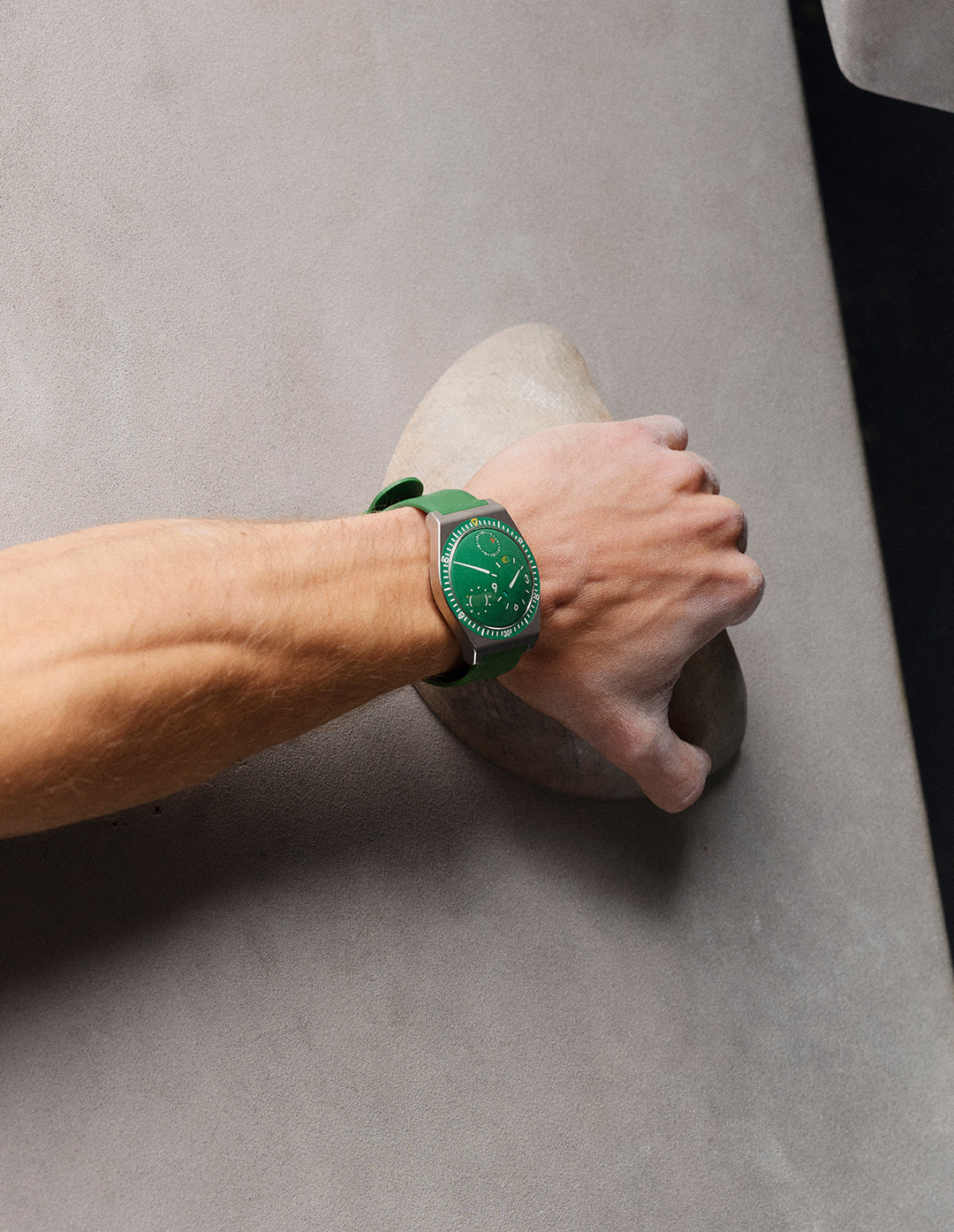Ressence TYPE 7 Cactus, a titanium GMT watch with a green dial, shown as worn by a person bouldering on a wall. Vertical image.