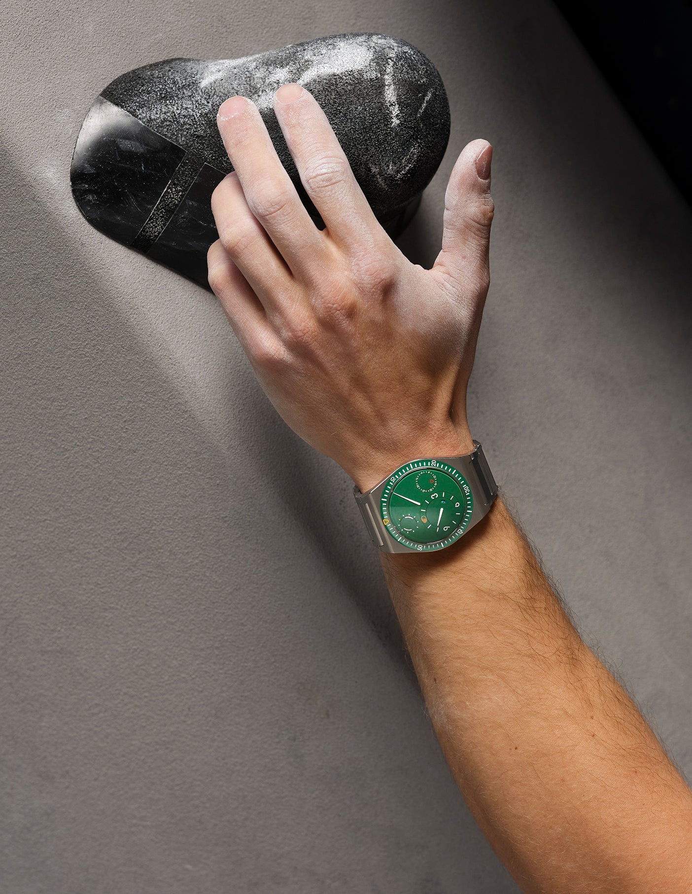 Hand wearing a cactus green Ressence TYPE 7 sport-chic GMT watch on a gray background, vertical image