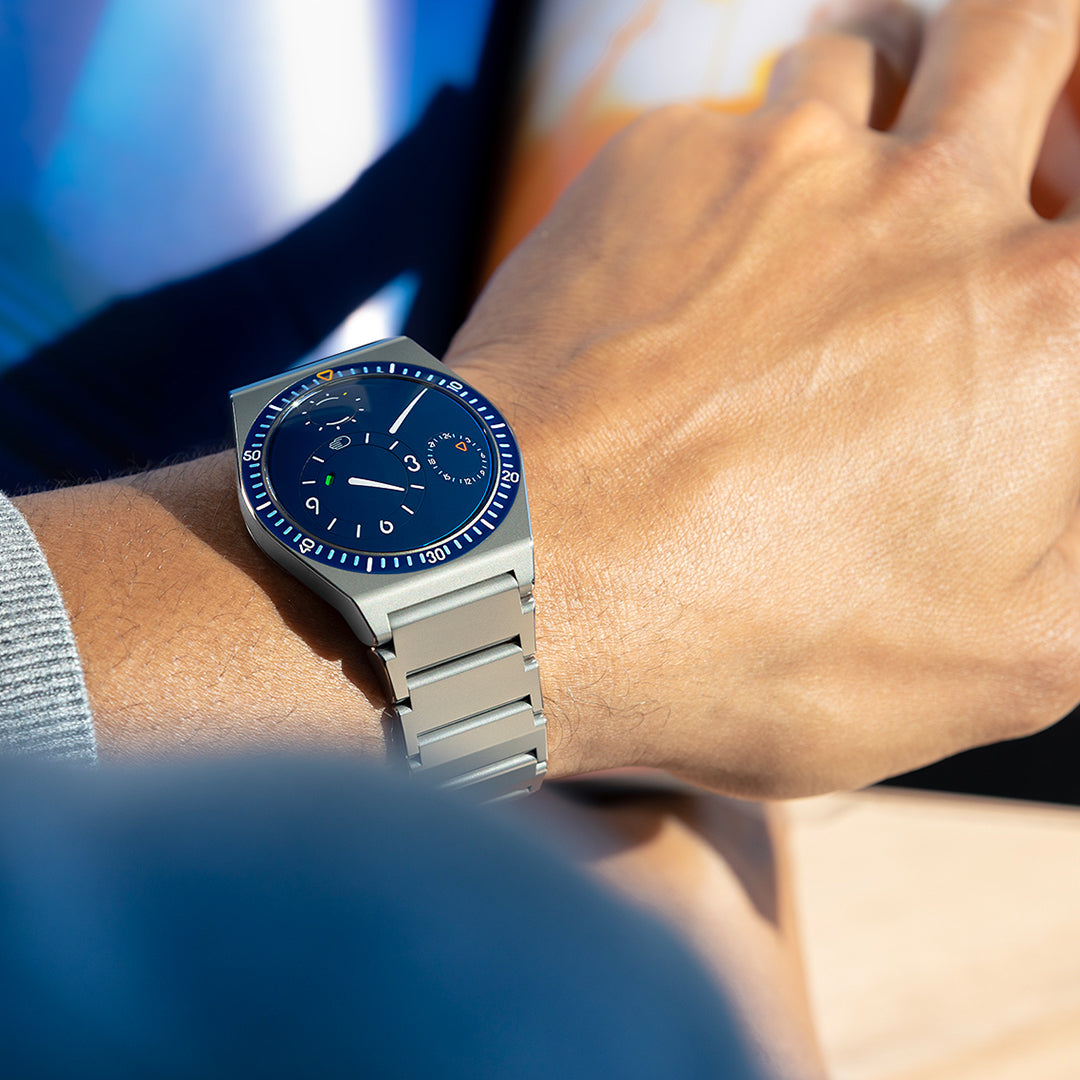 Close-up of a person's wrist wearing a night blue Ressence TYPE 7 sport-chic GMT watch with a titanium integrated bracelet, square image