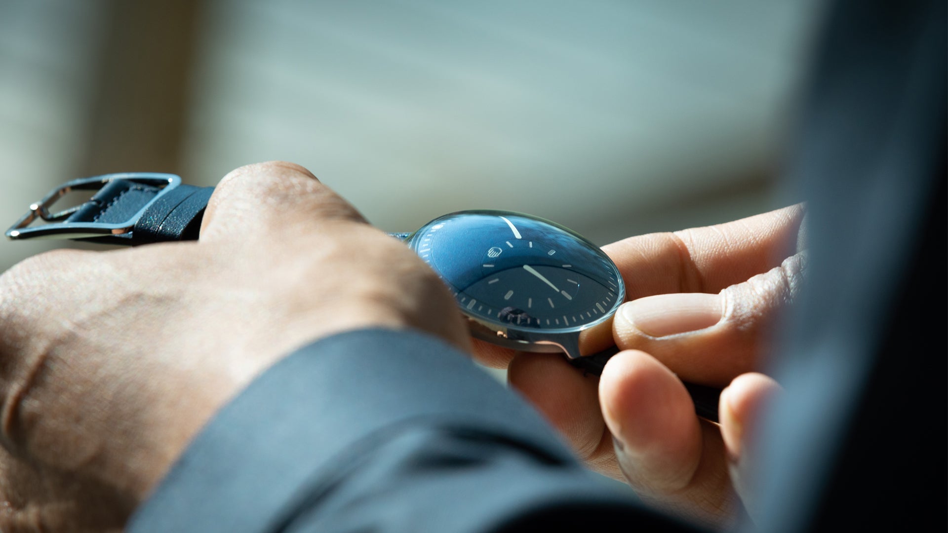Ressence TYPE 8 Cobalt Blue, a minimal design watch in titanium shown in the hands of a man admiring it, and displaying 10 minutes past 6 o'clock 