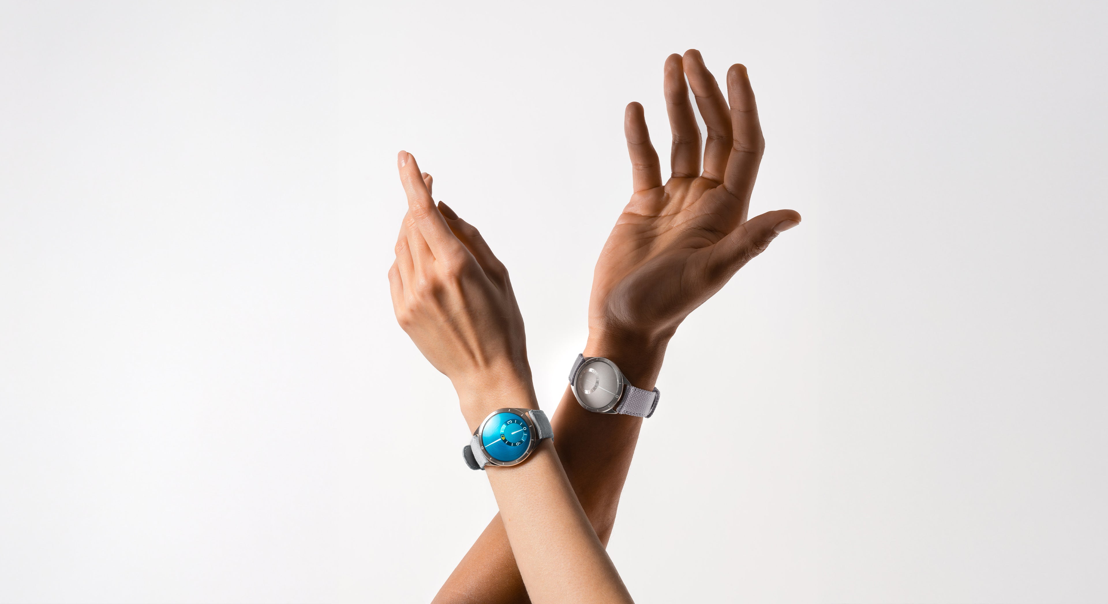 Two arms, one of a woman with a Ressence TYPE 9 Aqua and man's one with a Ressence TYPE 9 Grey both raised up, on a grey background
